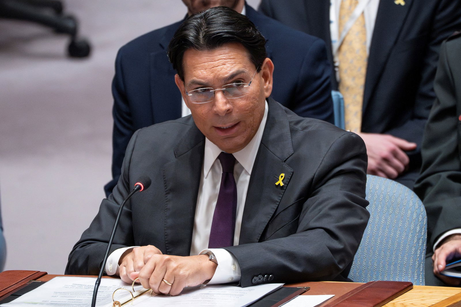 A man in a dark grey suit rests two fists on a desk