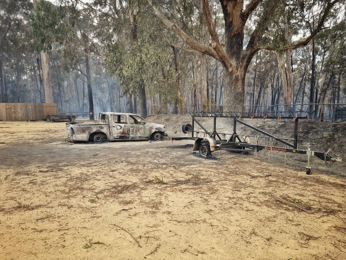 A burnt-out ute sits on a patch of smoky ground.