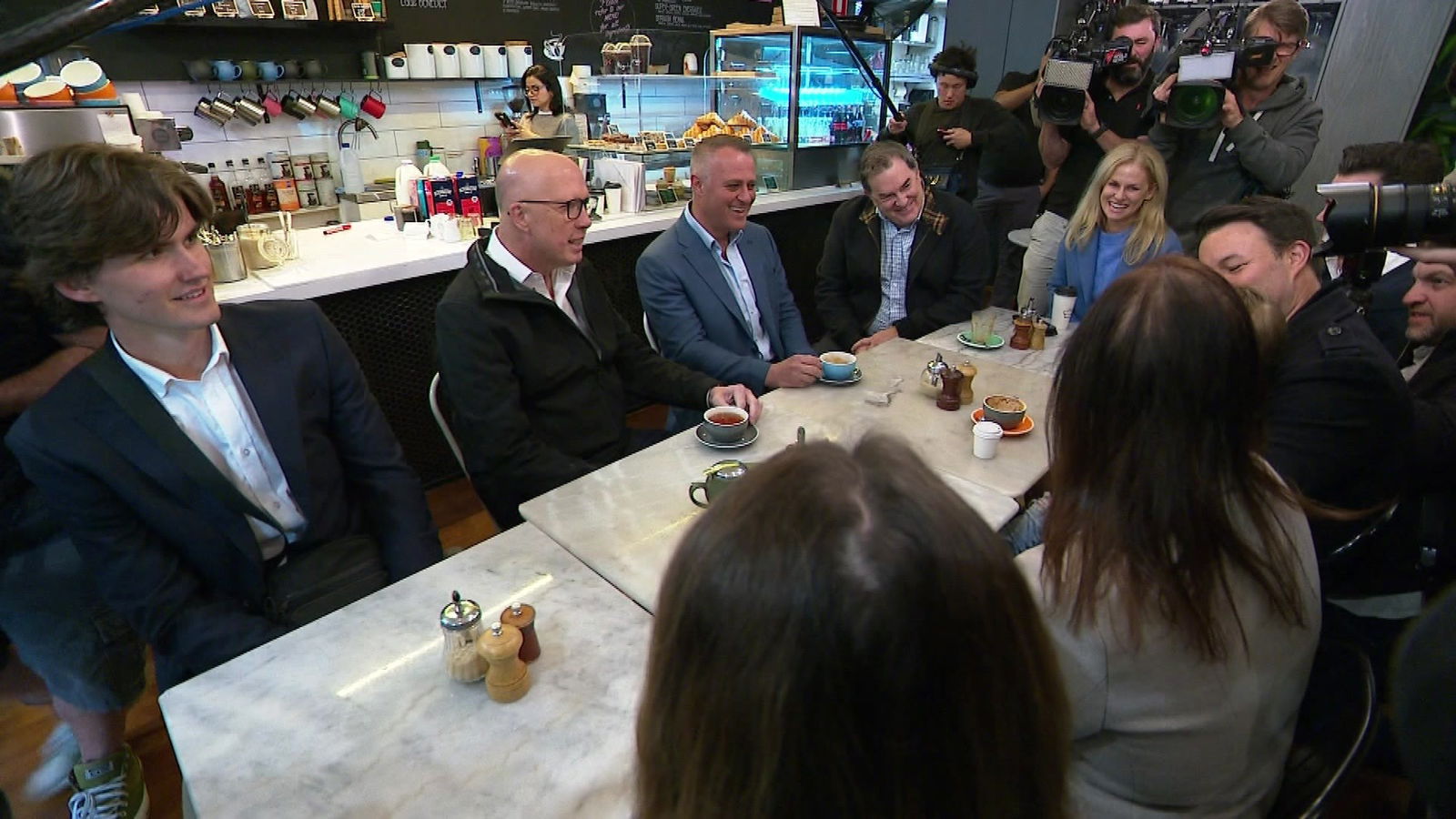 Peter Dutton sitting next to Tim Wilson at a cafe table surrounded by men and women