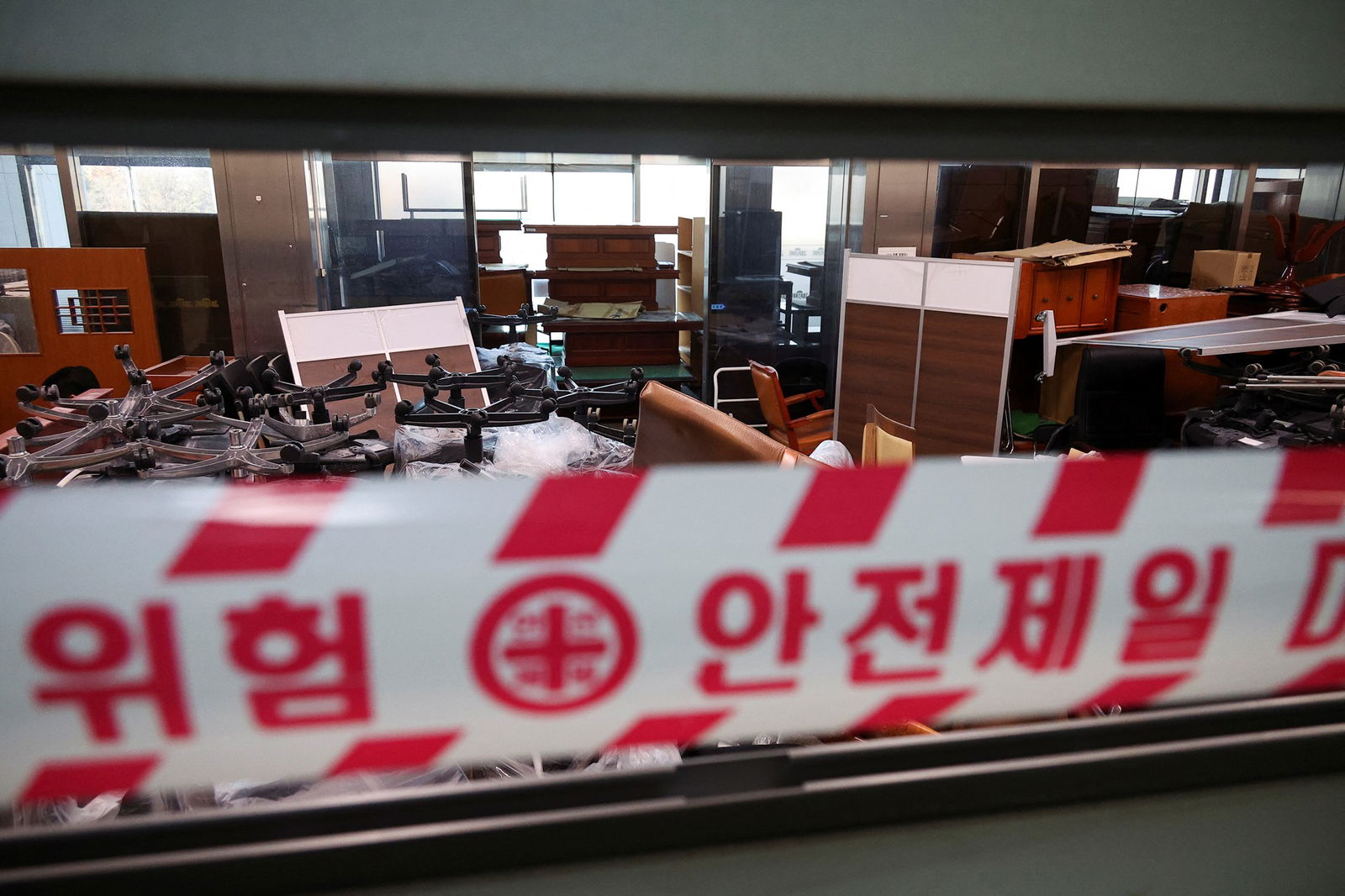 a red and white tape obscures part of an office room with furniture everywhere in heaps