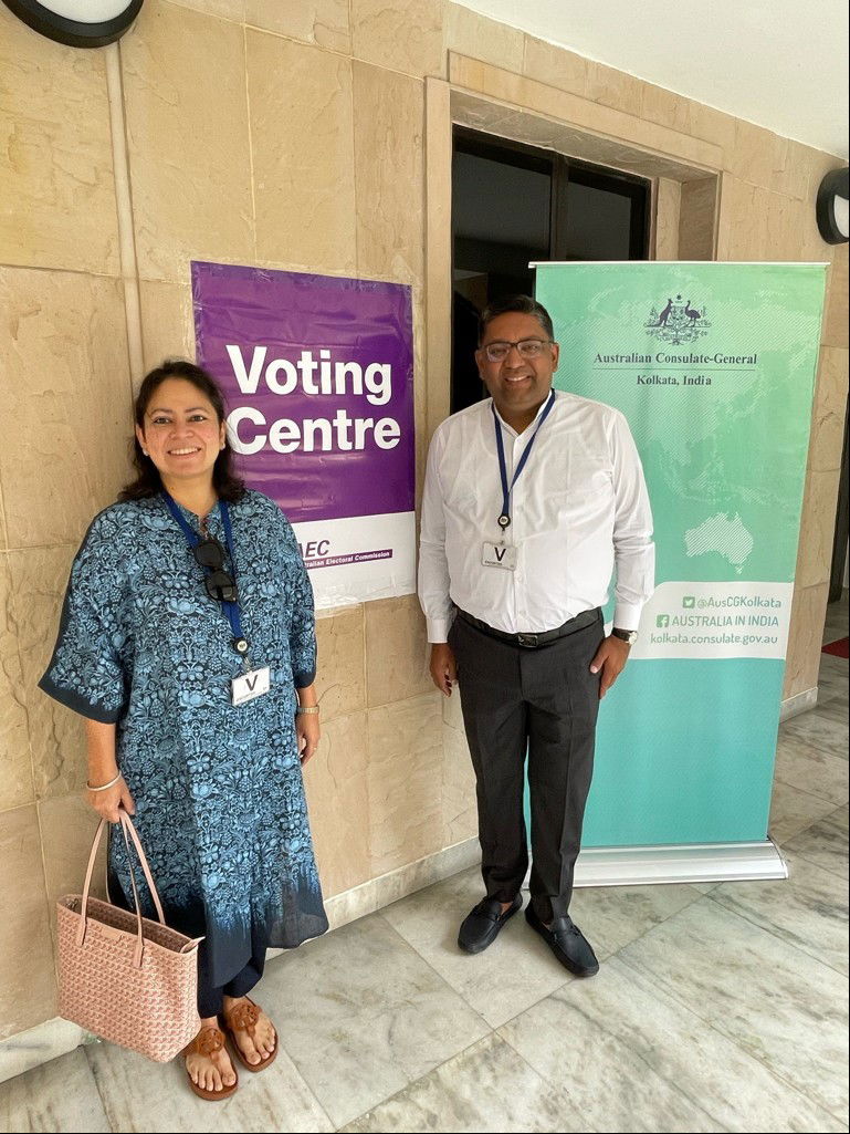 a man and a woman stand in front of a purple voting sign