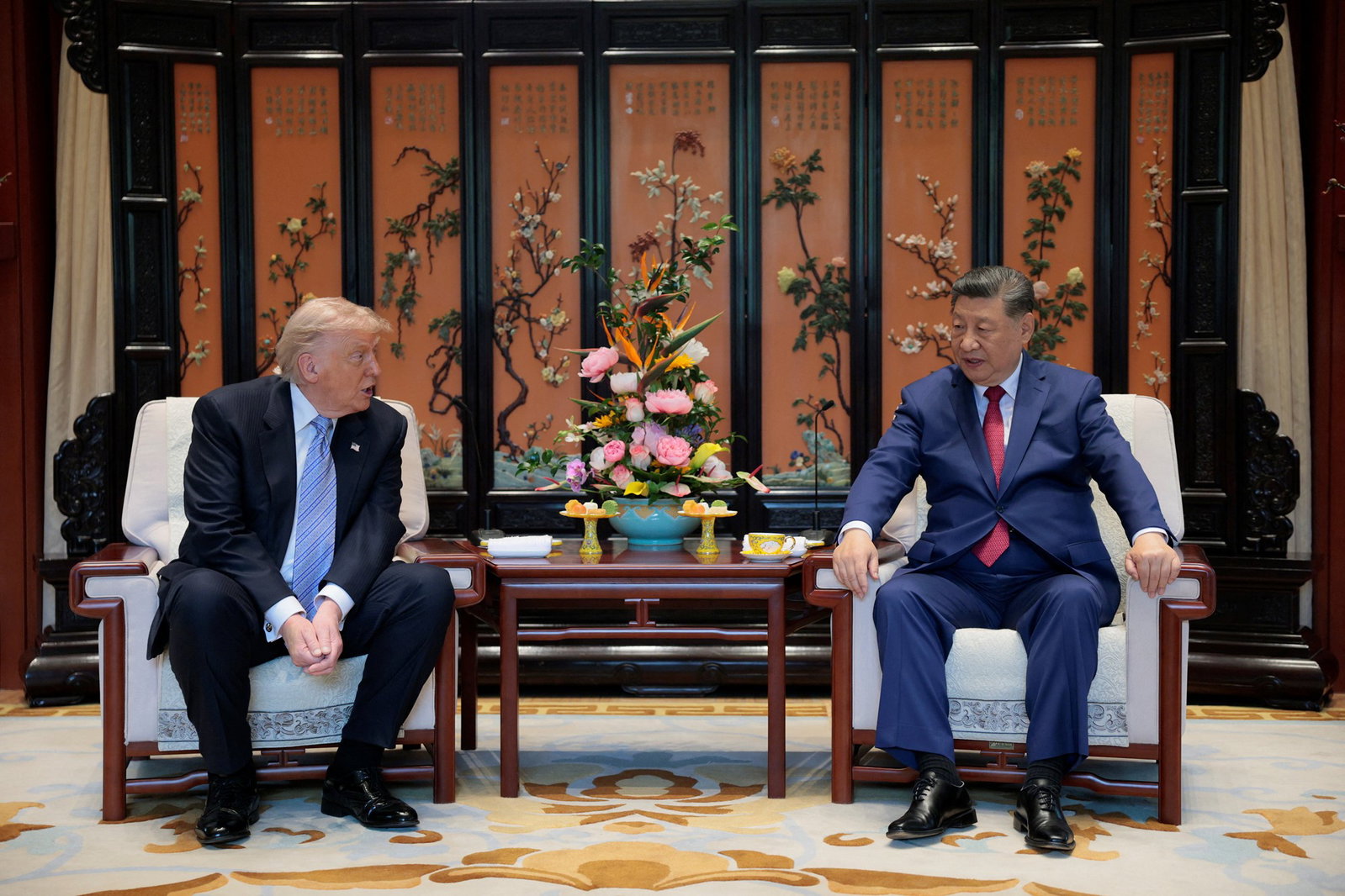 Two men in suits prepare sit down in an ornate room