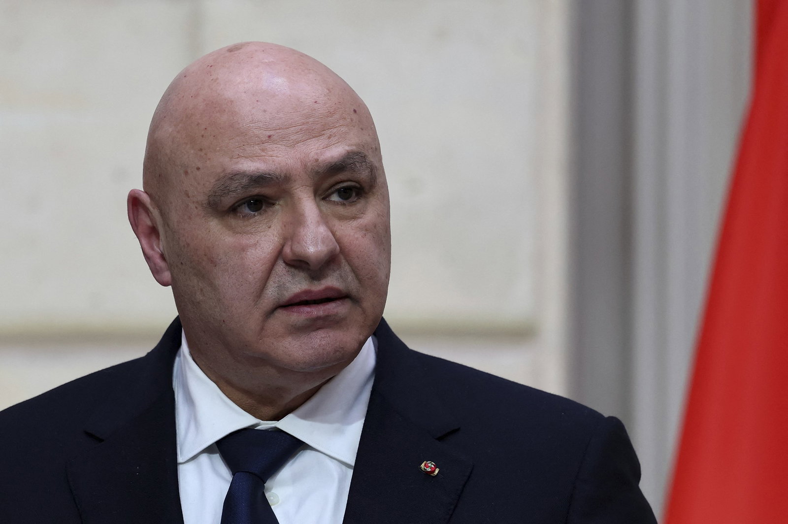 Un hombre calvo con traje negro mira a la cámara de la derecha.