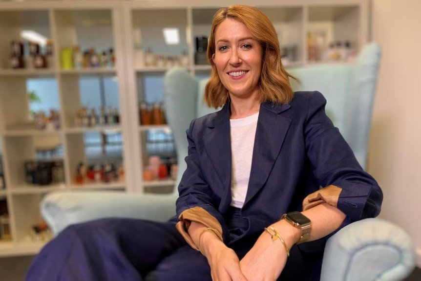Kate sitting in navvy blue suit on a couch in front of cosmetics.