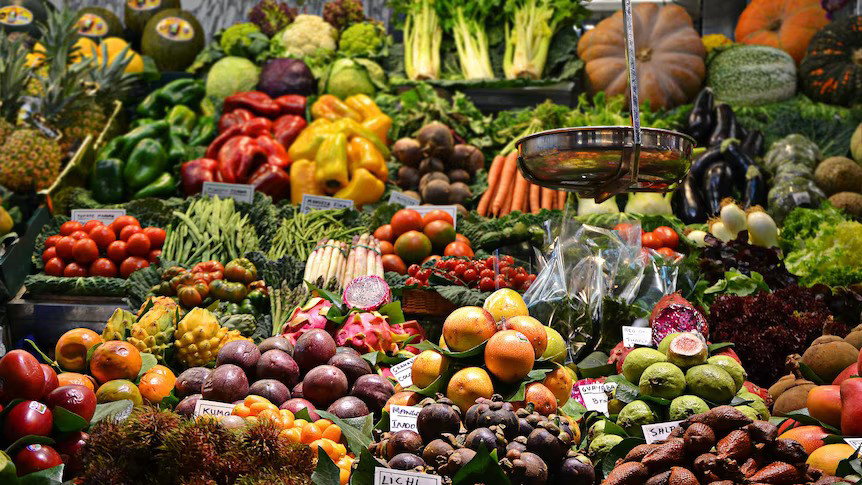 A colourful variety of fresh fruit and vegetables on display at a market. A scales hangs above on the right hand side