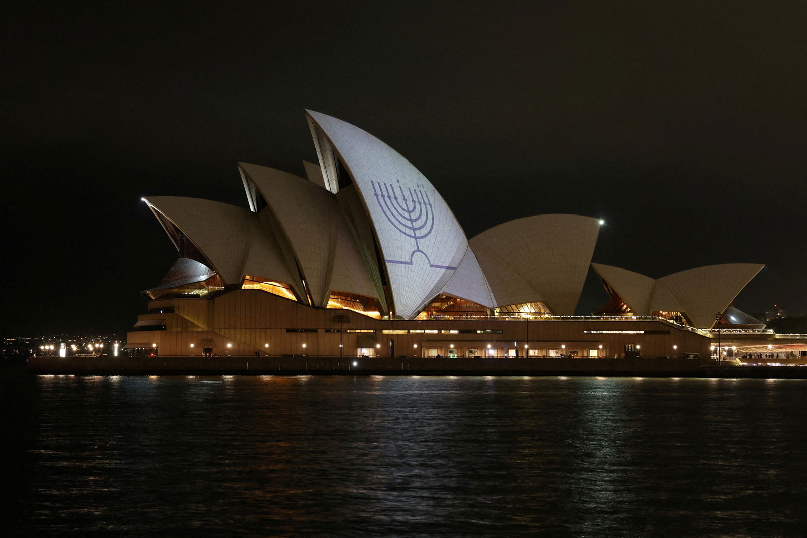 O telhado branco da Sydney Opera House é iluminado de branco com uma menorá azul