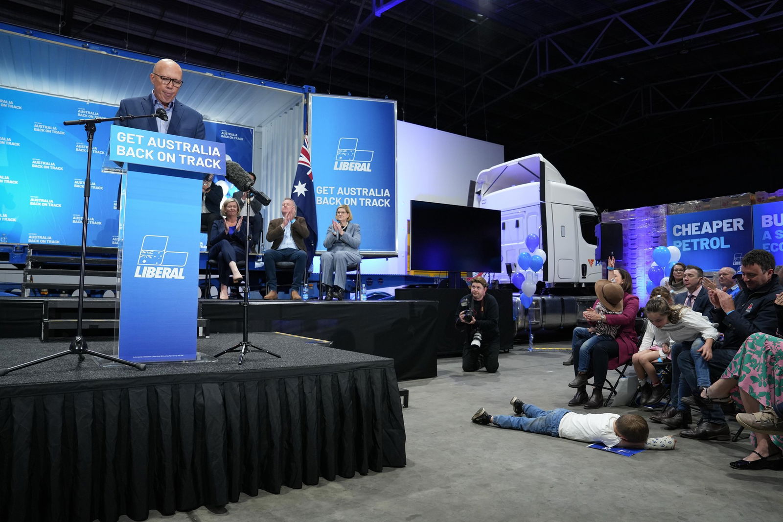 A boy lies face-down on the floor of a room in front of Peter Dutton