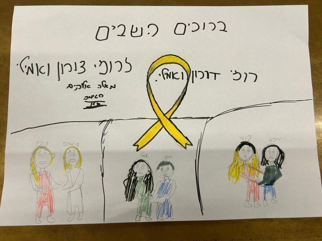 A child's drawing shows a yellow ribbon, some Hebrew writing and three drawings of people holding hands.