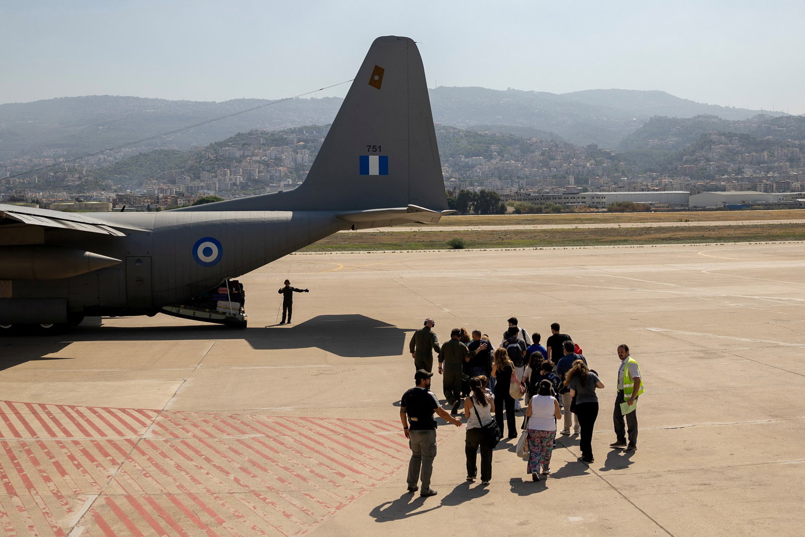 a group of people move towards the back opening of an airforce plane on a bright tarmac