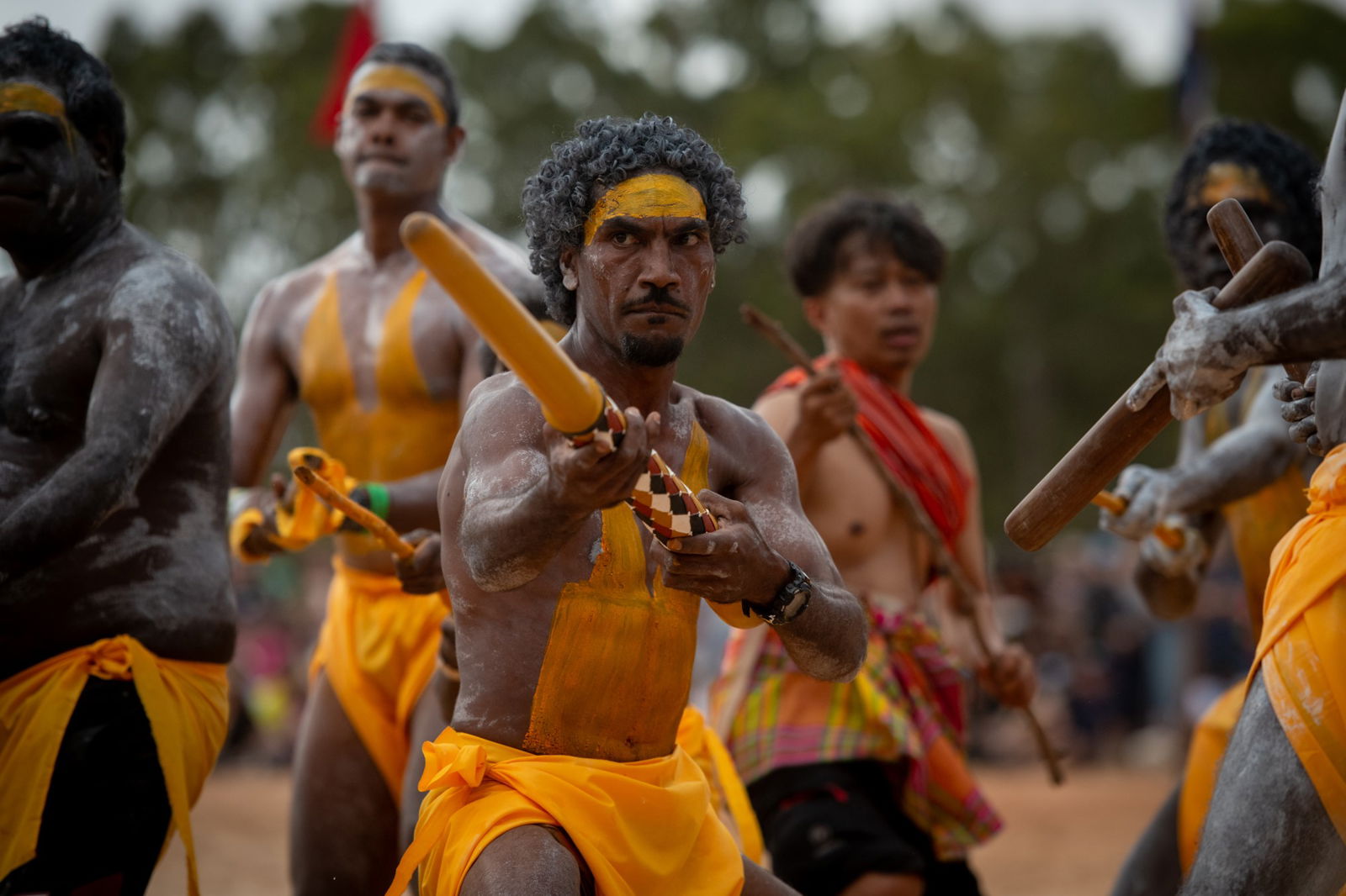 An Indigenous man points a painted stick.