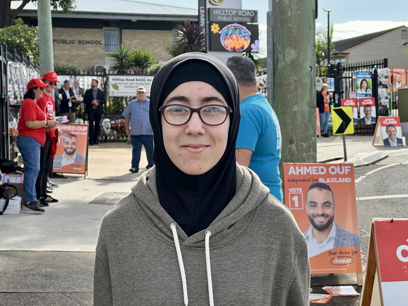 woman smiles at the camera while wearing a grey jumper and a black hijab