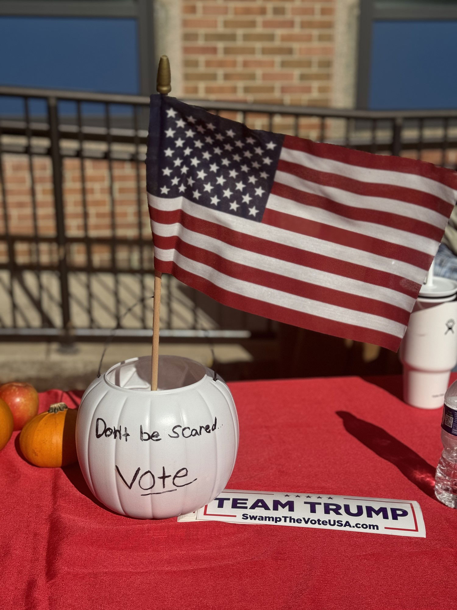 A table with a red cloth with a plastic pumpkin with Don't be scared, Vote written on it.