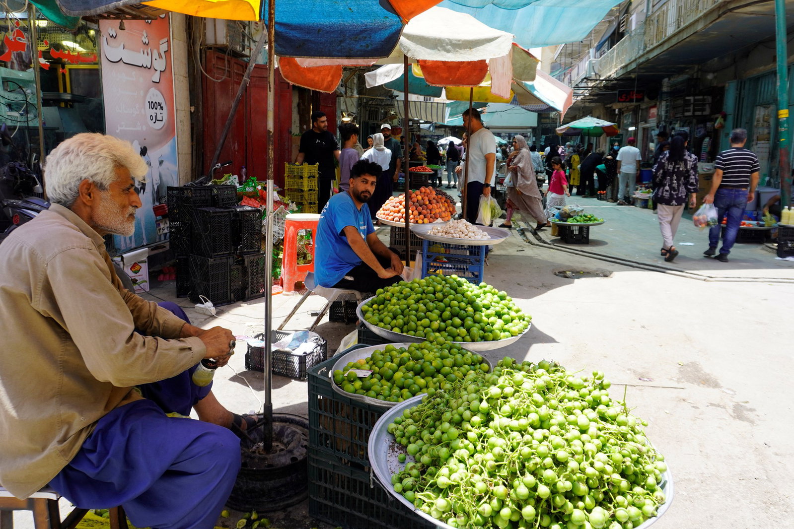 A man sits at a stall selling big trays of fruit