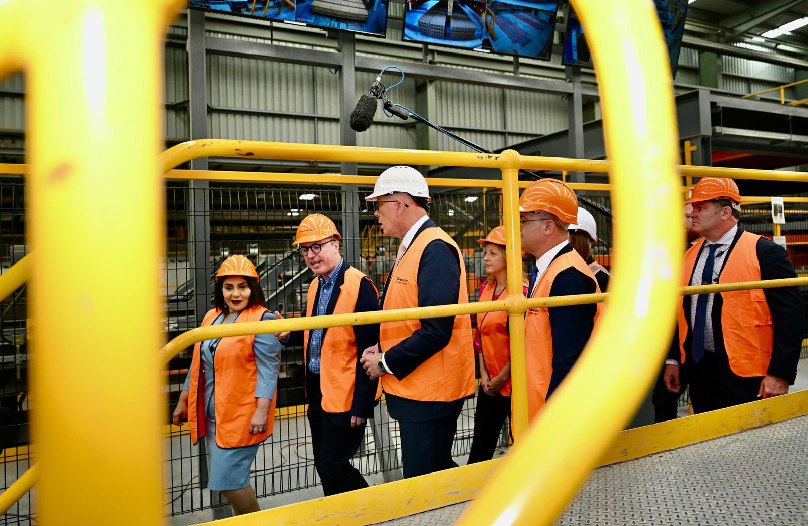 A group of people wearing hi-vis vests walk along scaffolding