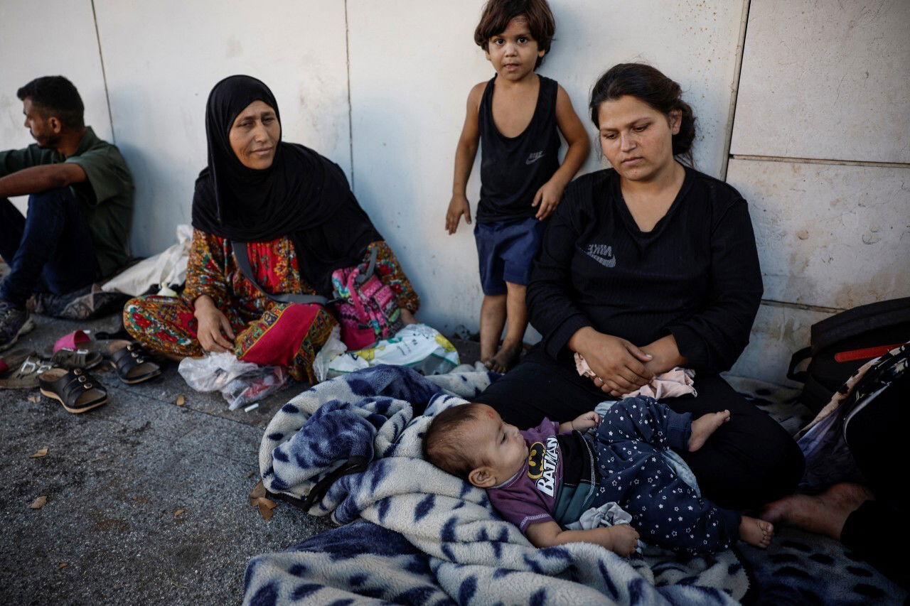 A group of women and children sit on the ground.