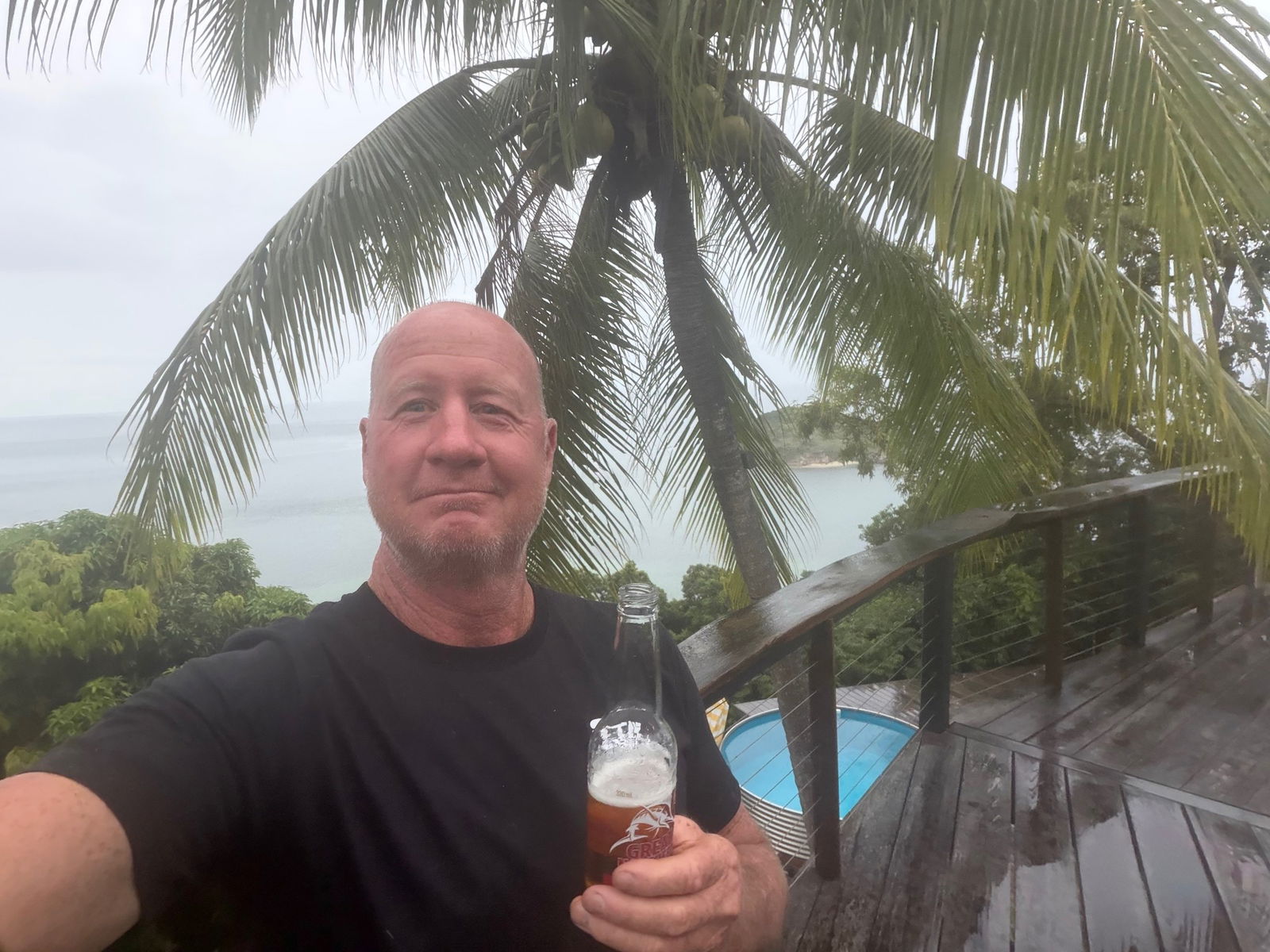 A man taking a selfie holding a beer with the ocean in the background