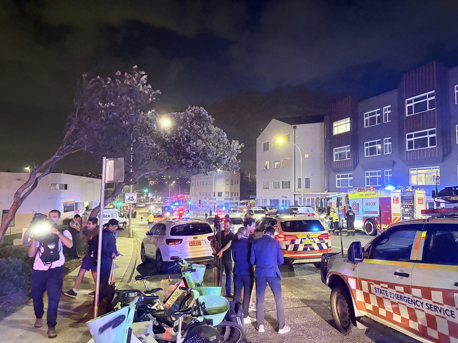 Media stand on the side of a road at night near police cars