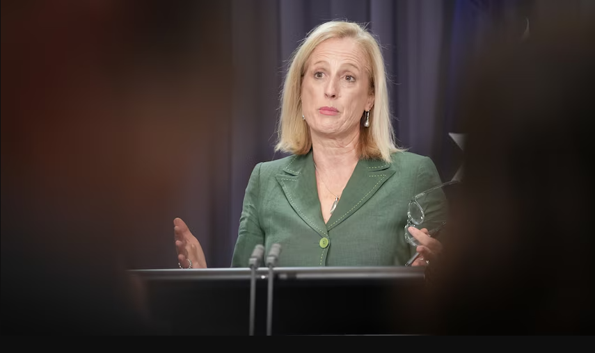 A woman in a green blazer stands behind a podium