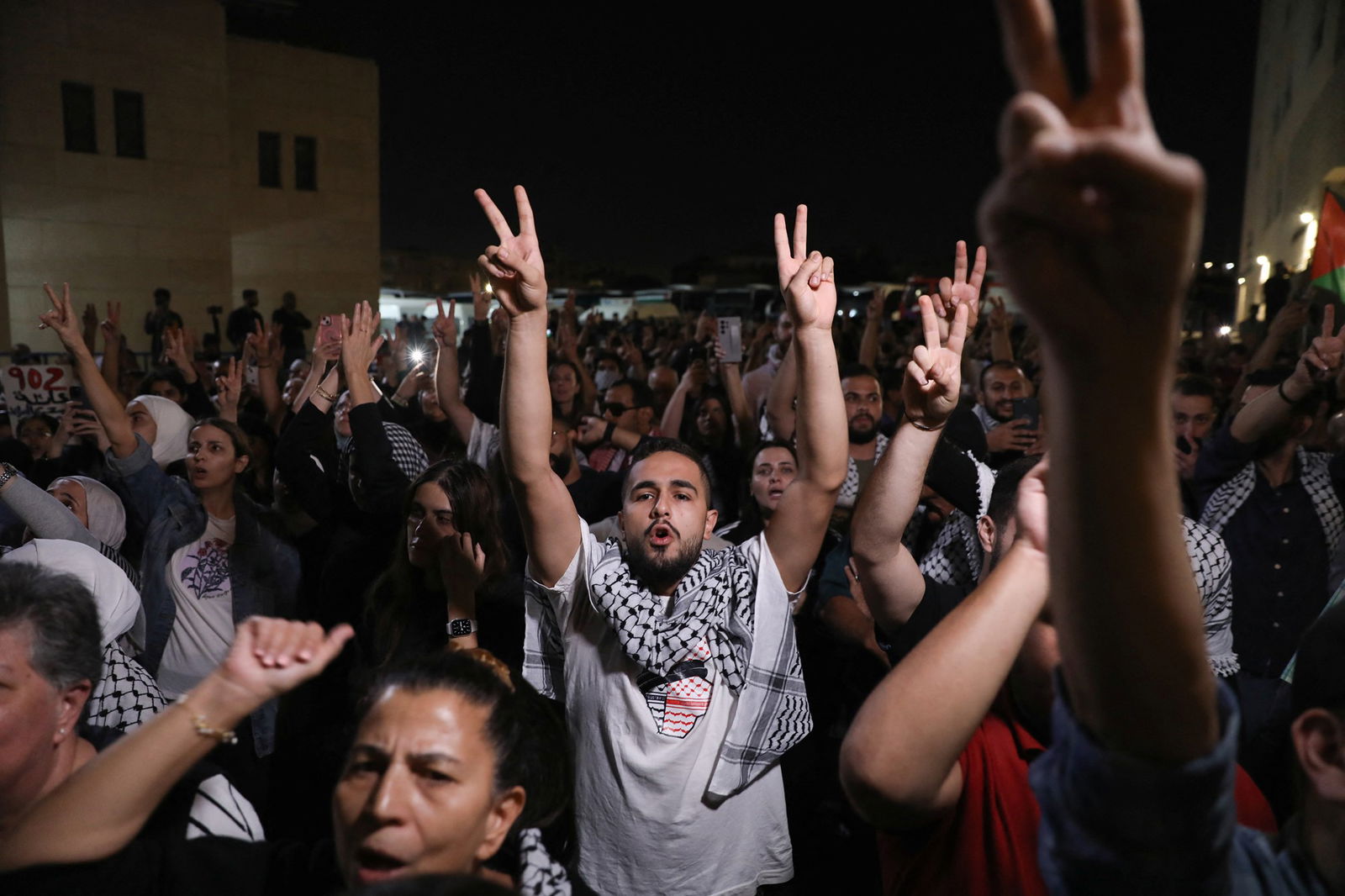 A man giving two peace signs in a crowd. 