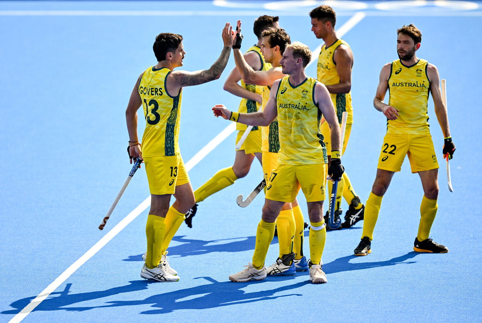 A group of Australian hockey players wearing gold and green uniforms celebrate.