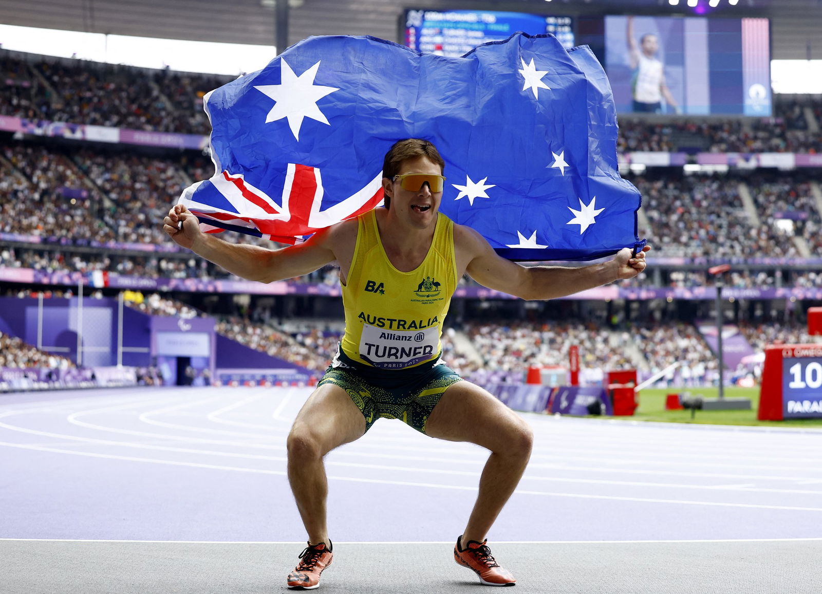 Australian Para athlete James Turner squats holding an Australian flag behind his back after winning a gold medal.