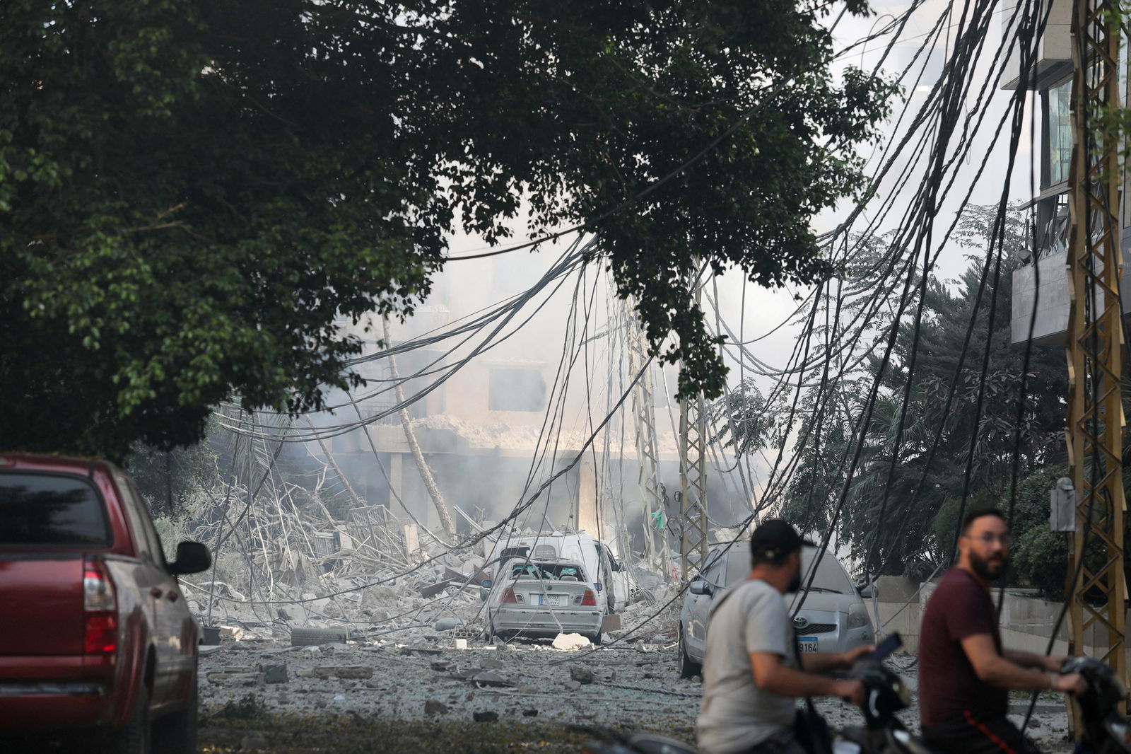 Two people walk past a street filled with debris; power lines down