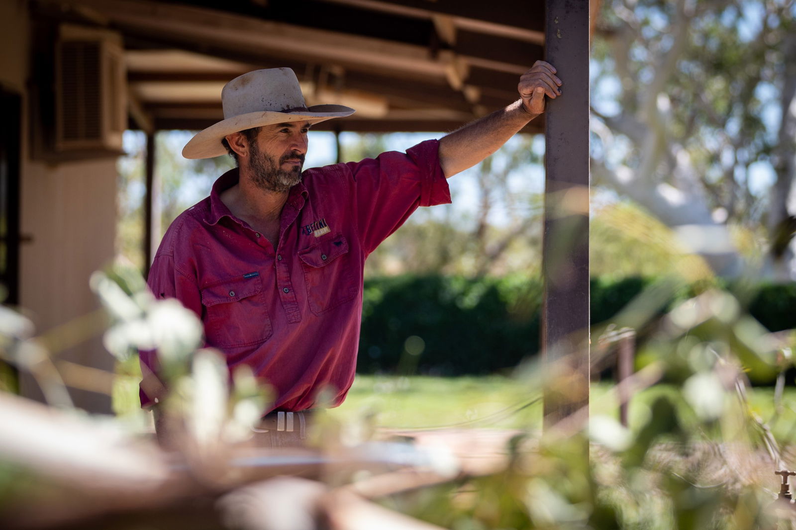 A man in a cowboy hat leans against a verandah post