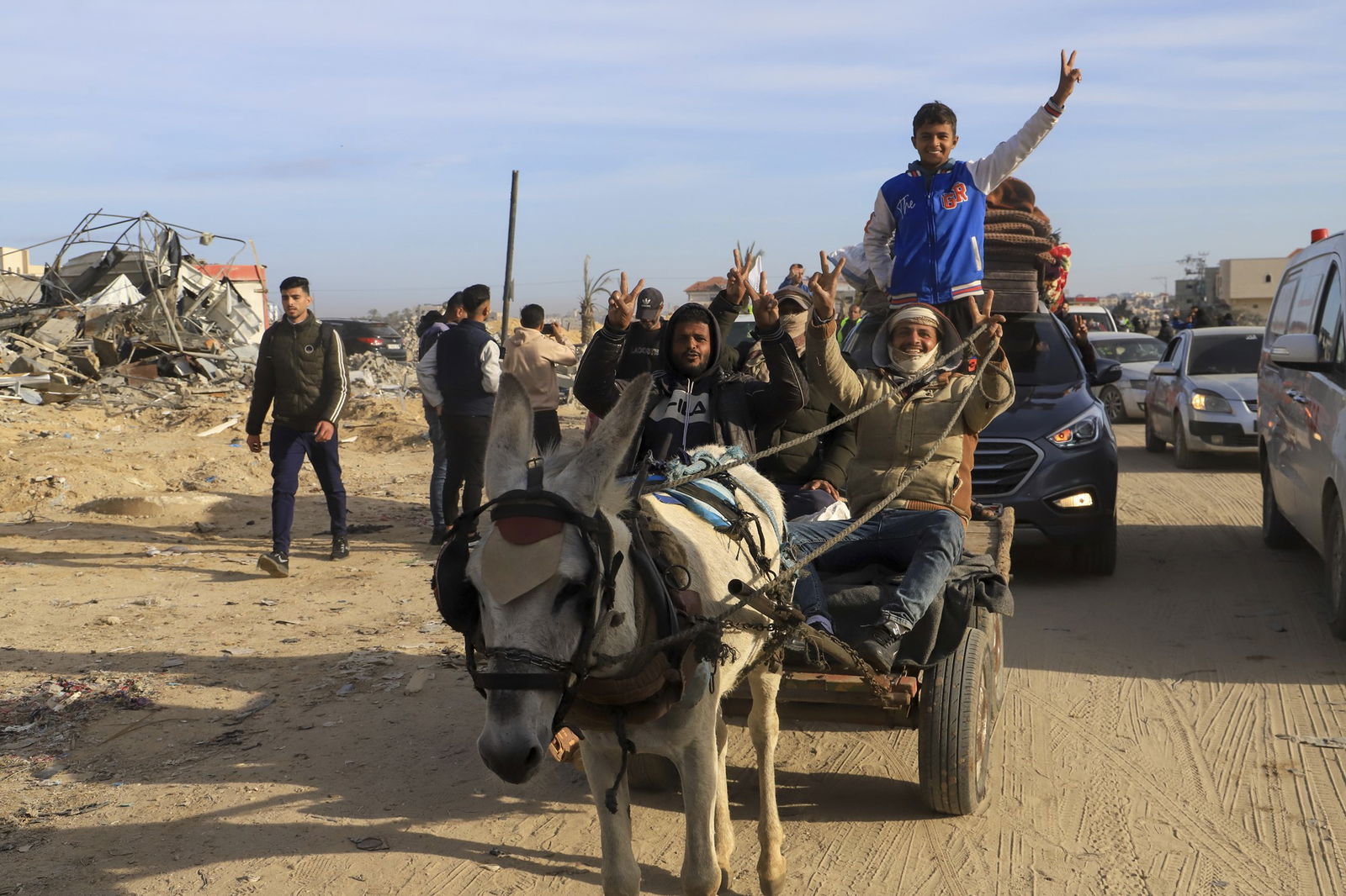 Displaced Palestinians flash V-sign as they ride a donkey through a destroyed neighbourhood.