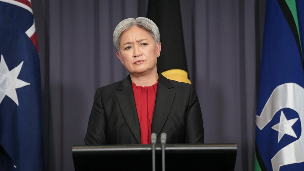 Penny Wong looks at a reporter while standing in front of a lectern at a press conference in parliament house.