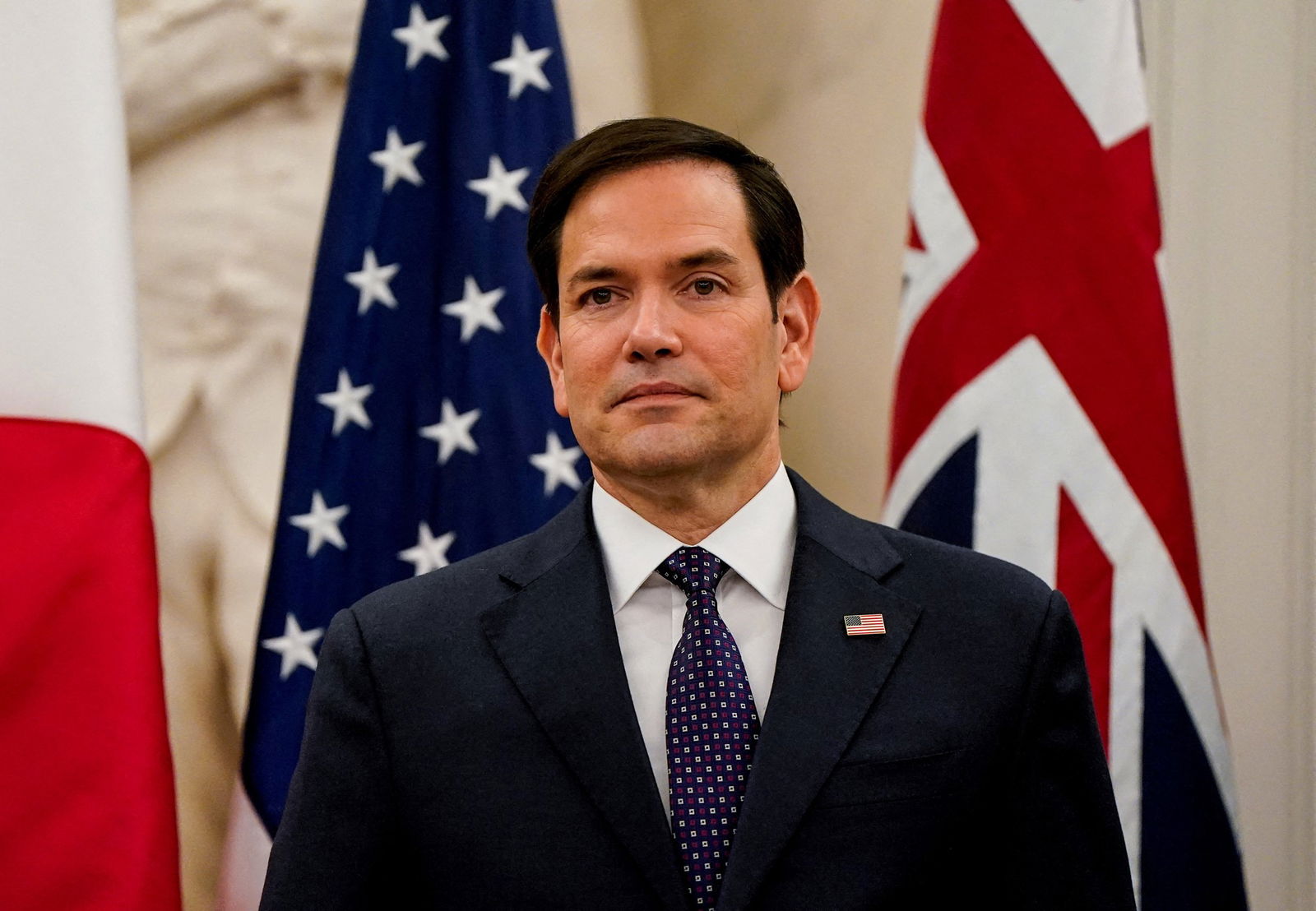 Marco Rubio standing in front of American flags.