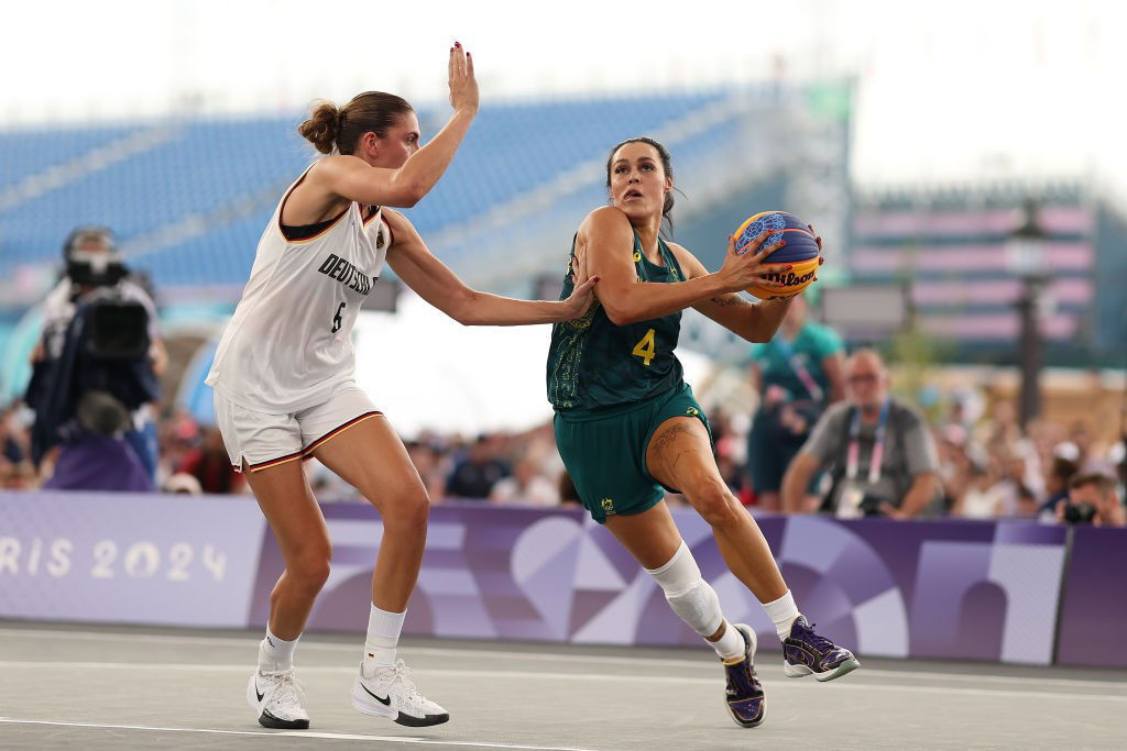 A basketballer in green swerves to pass a taller player in  white.