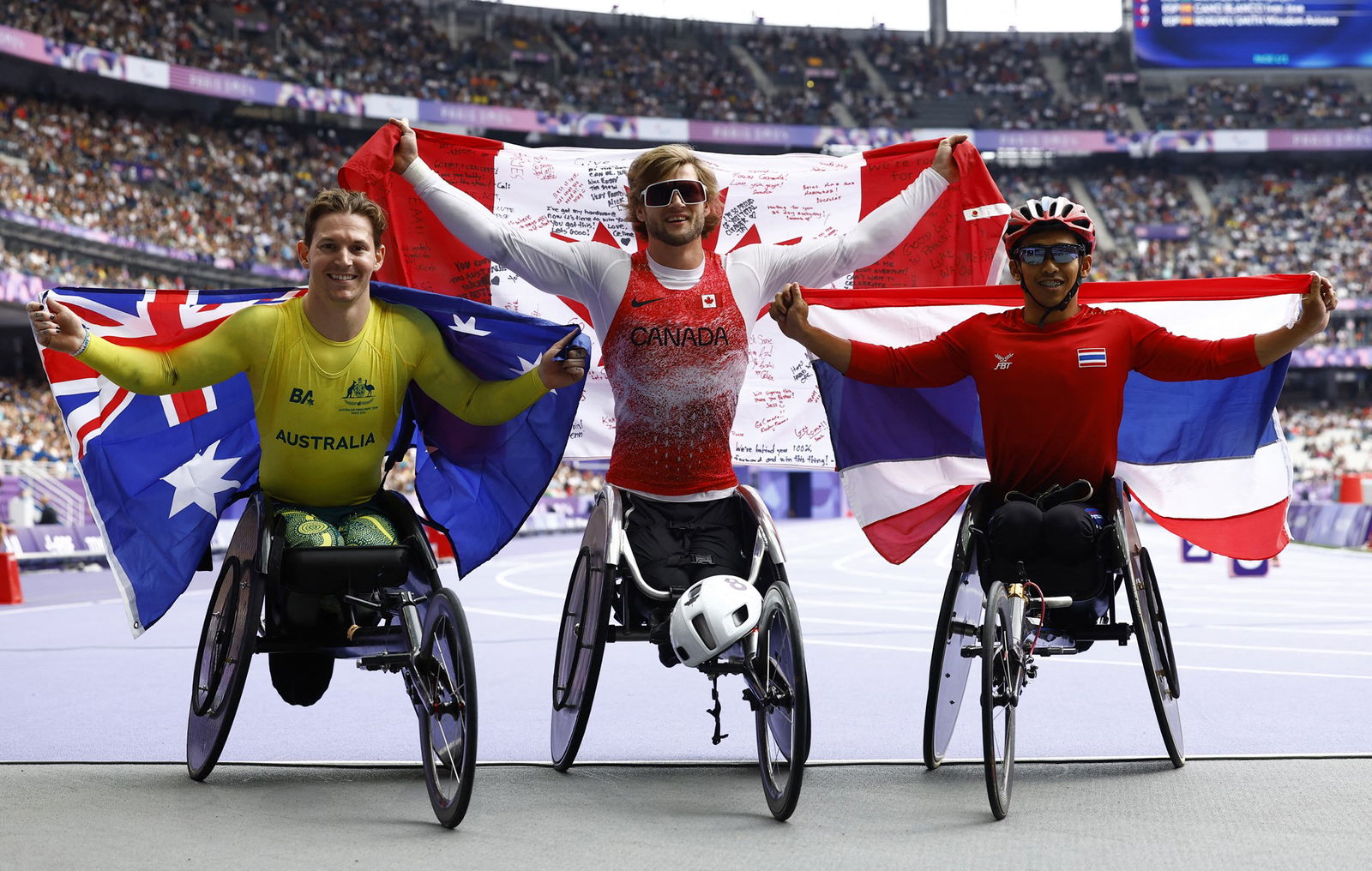 Three male wheelchair track racers pose with their country's flags and smile.