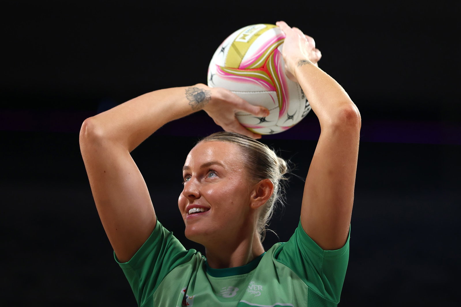 A player smiles and holds the ball over her head with both hands as she aims to shoot.