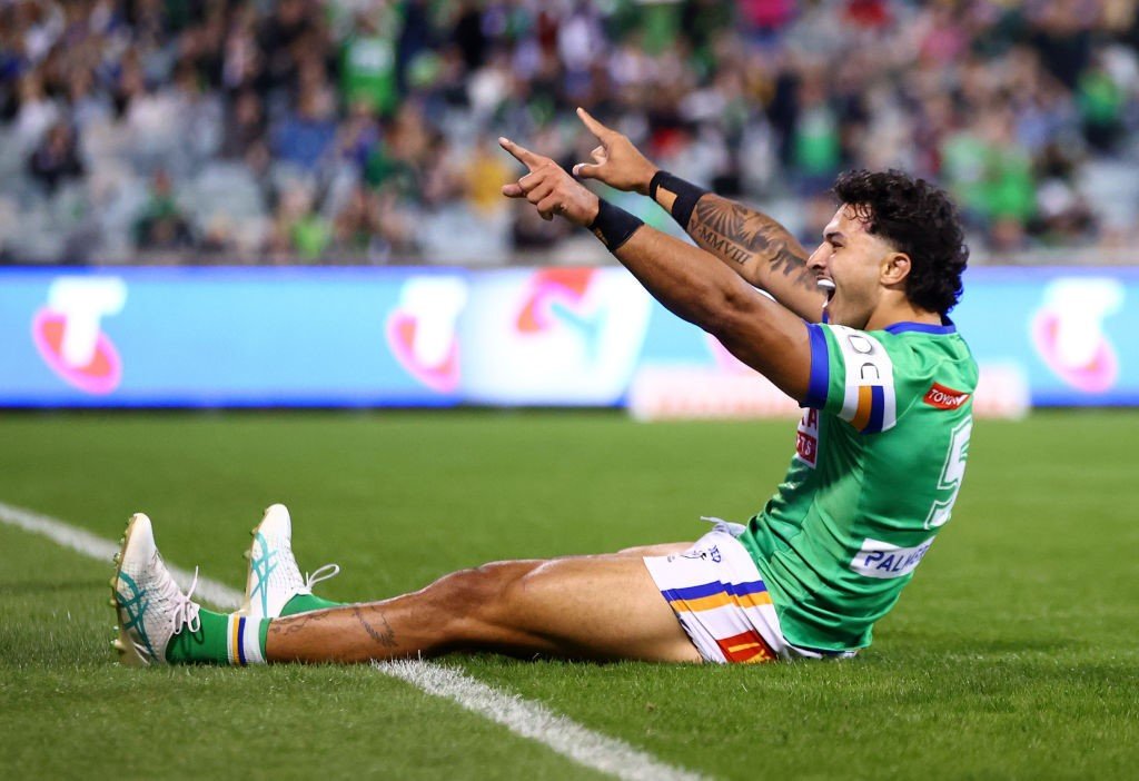 Xavier Savage sits on the ground and points to the sky after a try in an NRL game.