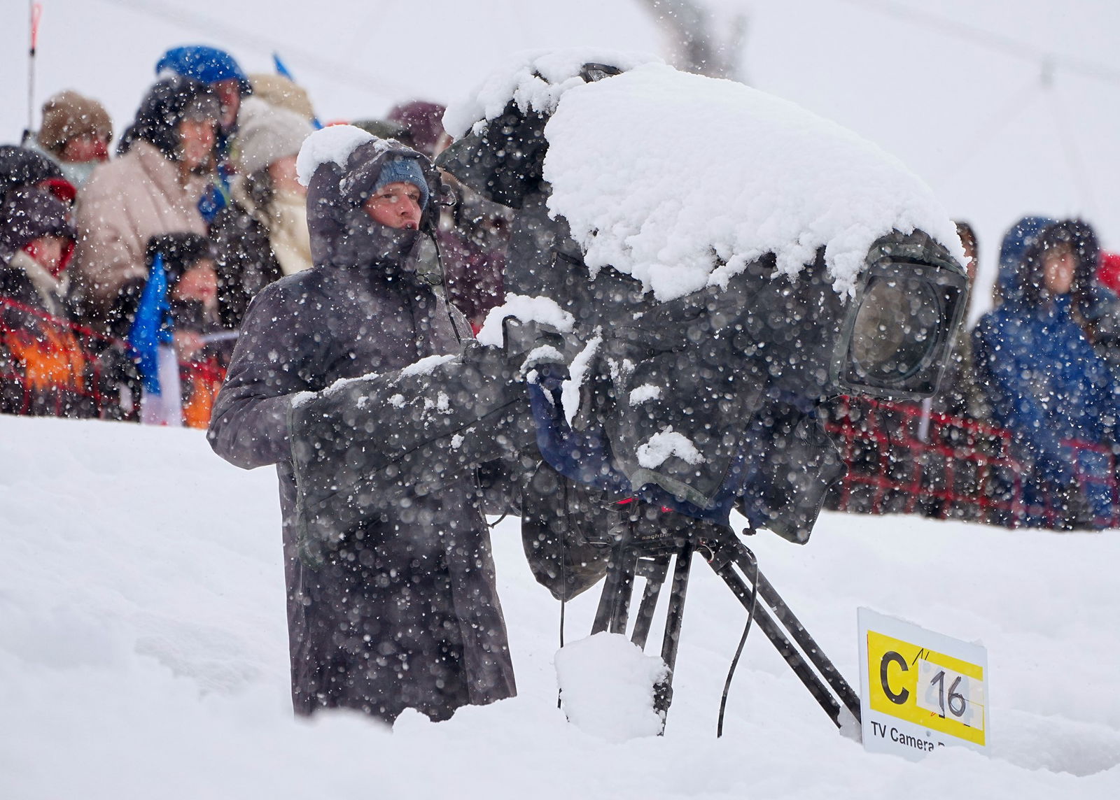 19 February 2026, Italy, Bormio: Olympia, Olympic Winter Games Milan Cortina 2026, ski mountaineering, sprint, semi-final, a cameraman stands on the track with a TV camera in heavy snowfall.