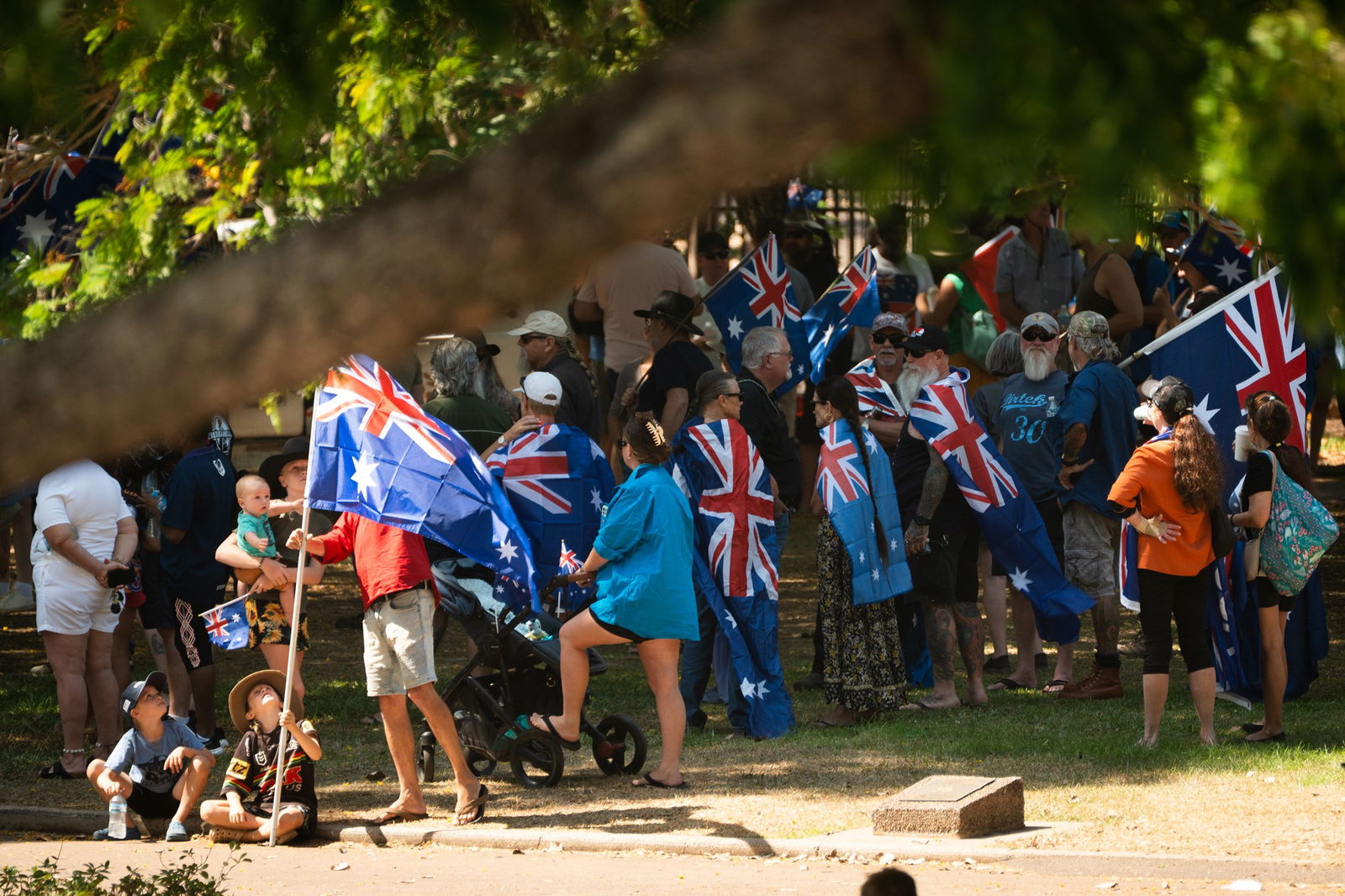 Una multitud de personas que sostienen una bandera australiana, algunas con ella cubiertas sobre su espalda como una capa, fotot tomada desde la distancia.