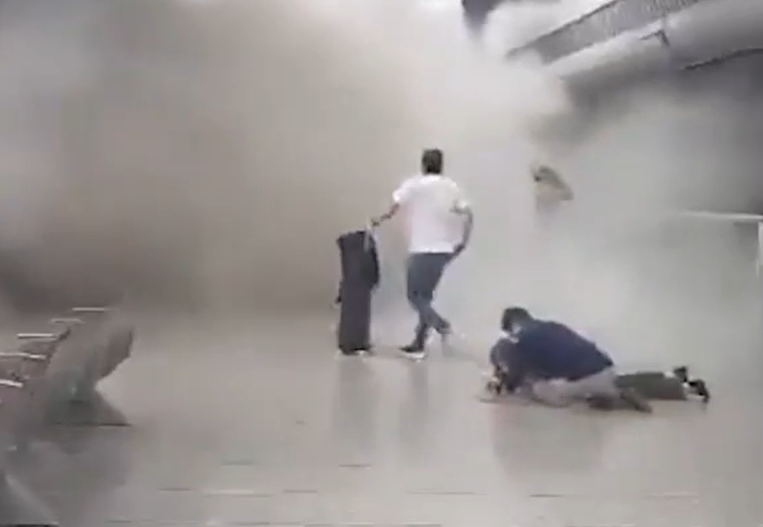 People running through a smoke-filled airport hallway.