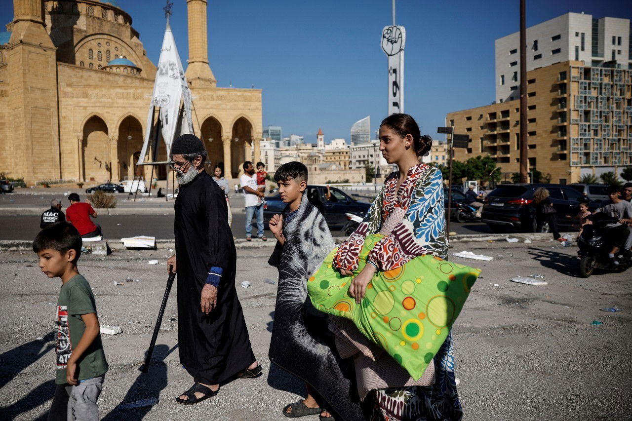 A group of people walk with various possessions.