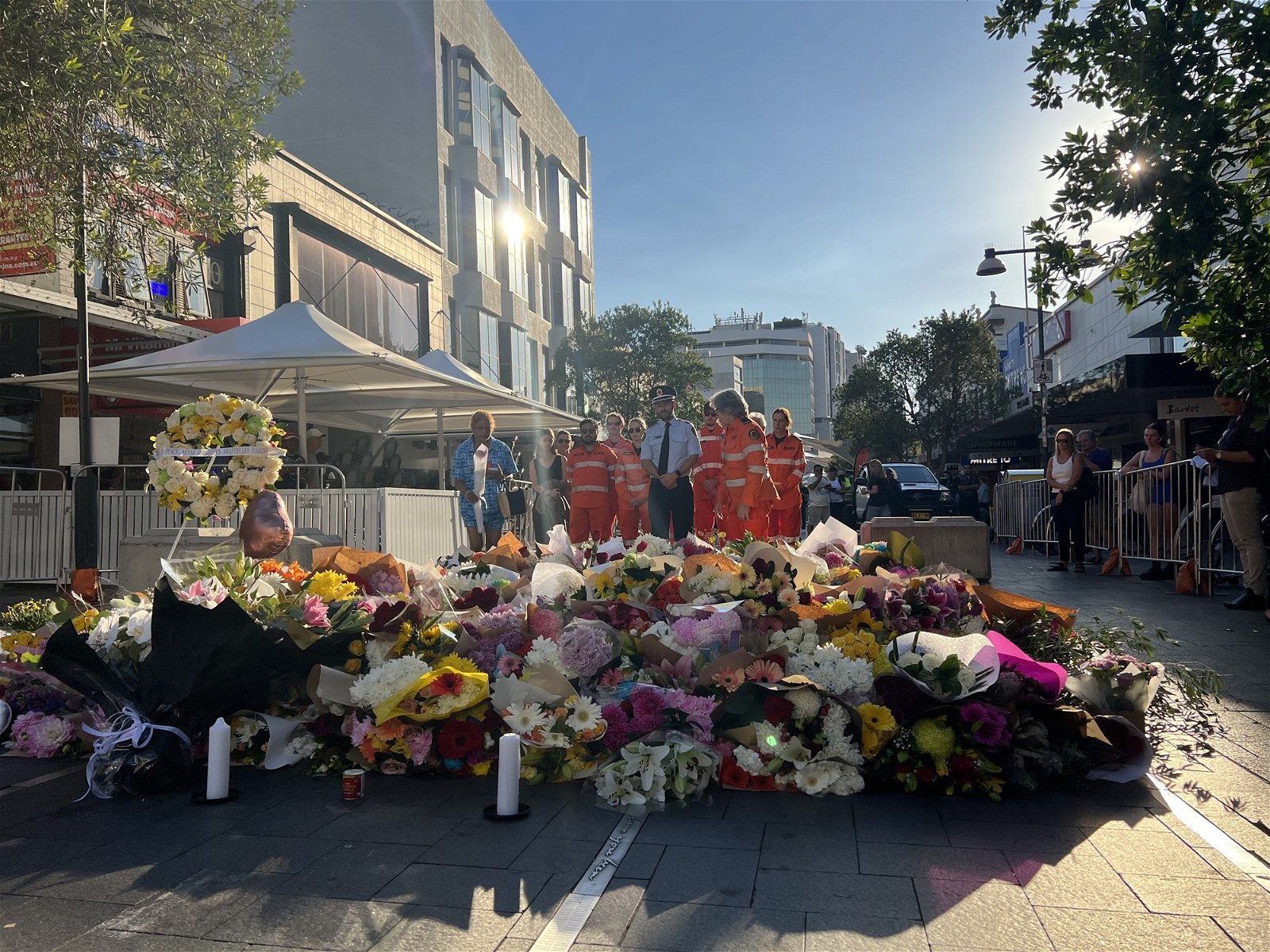 A group of people in fluro orange jumpsuits stand next to a bunch of flowers.