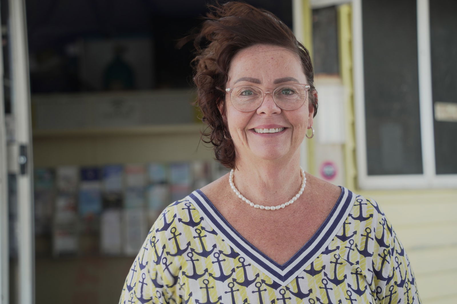 A head shot of Tanya Groom smiling to the camera, wearing a bright yellow top with anchors.