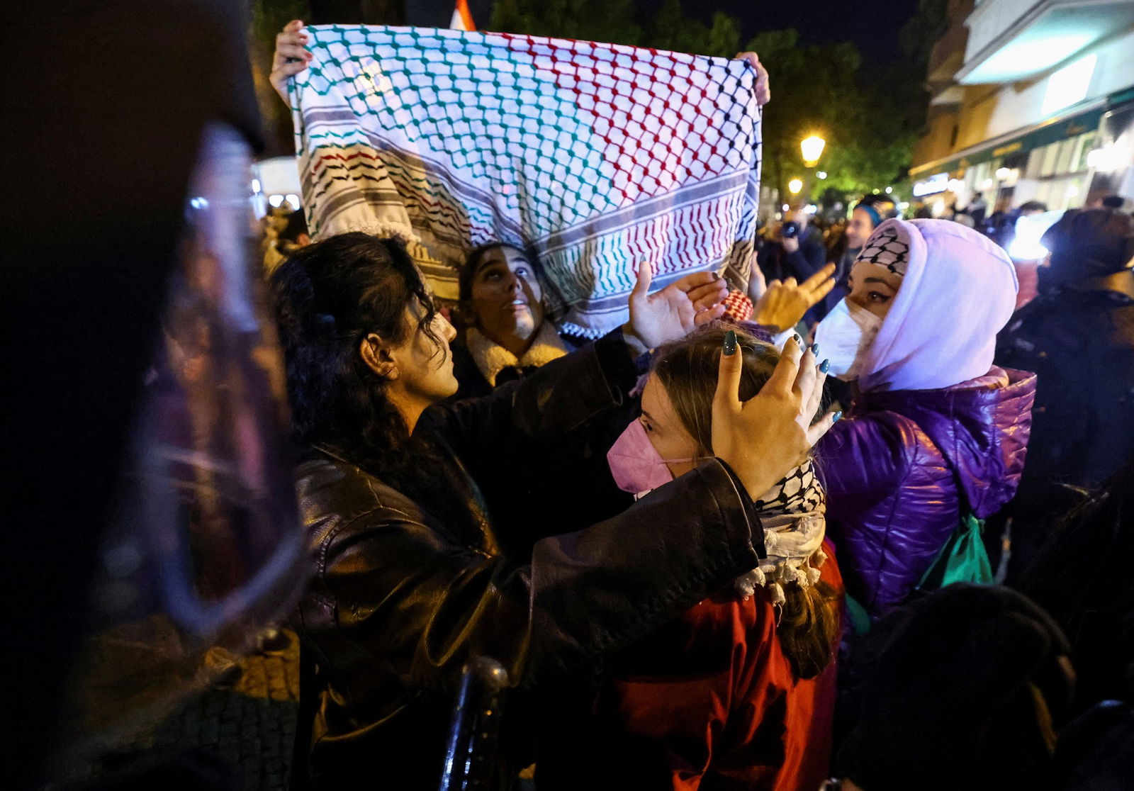 A woman holds a scarf above another.