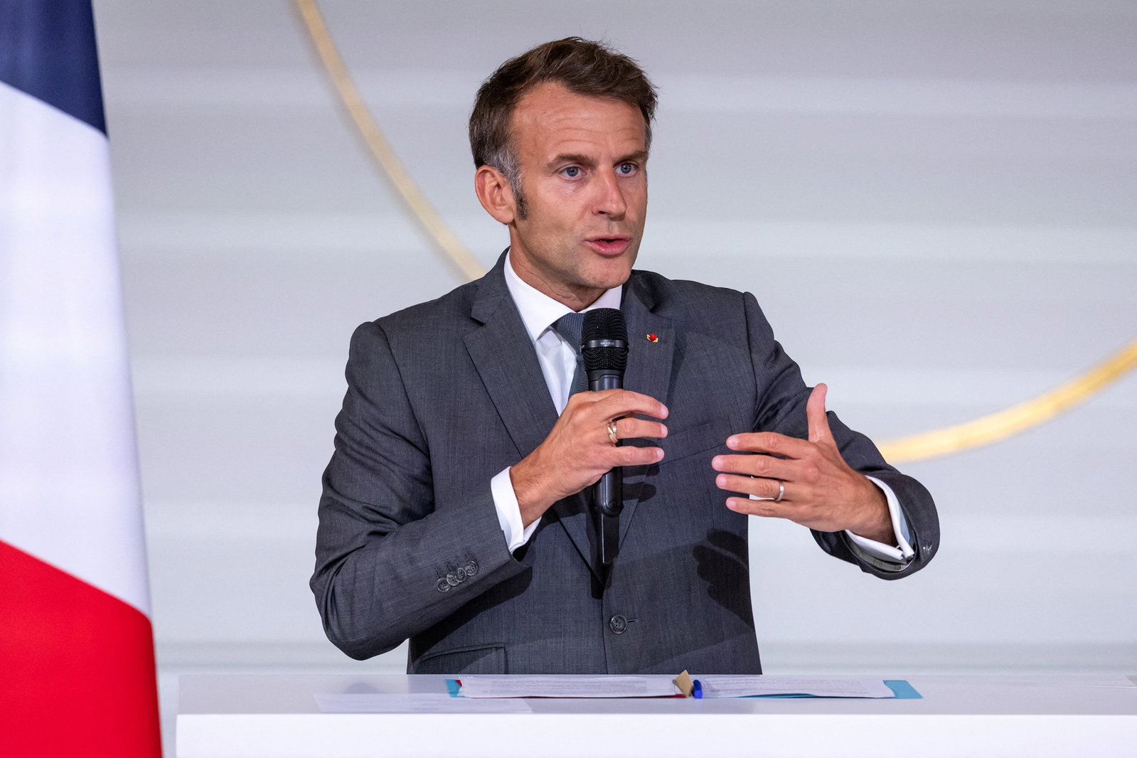 Emmanuel Macron, wearing a grey suit, talks into a microphone.