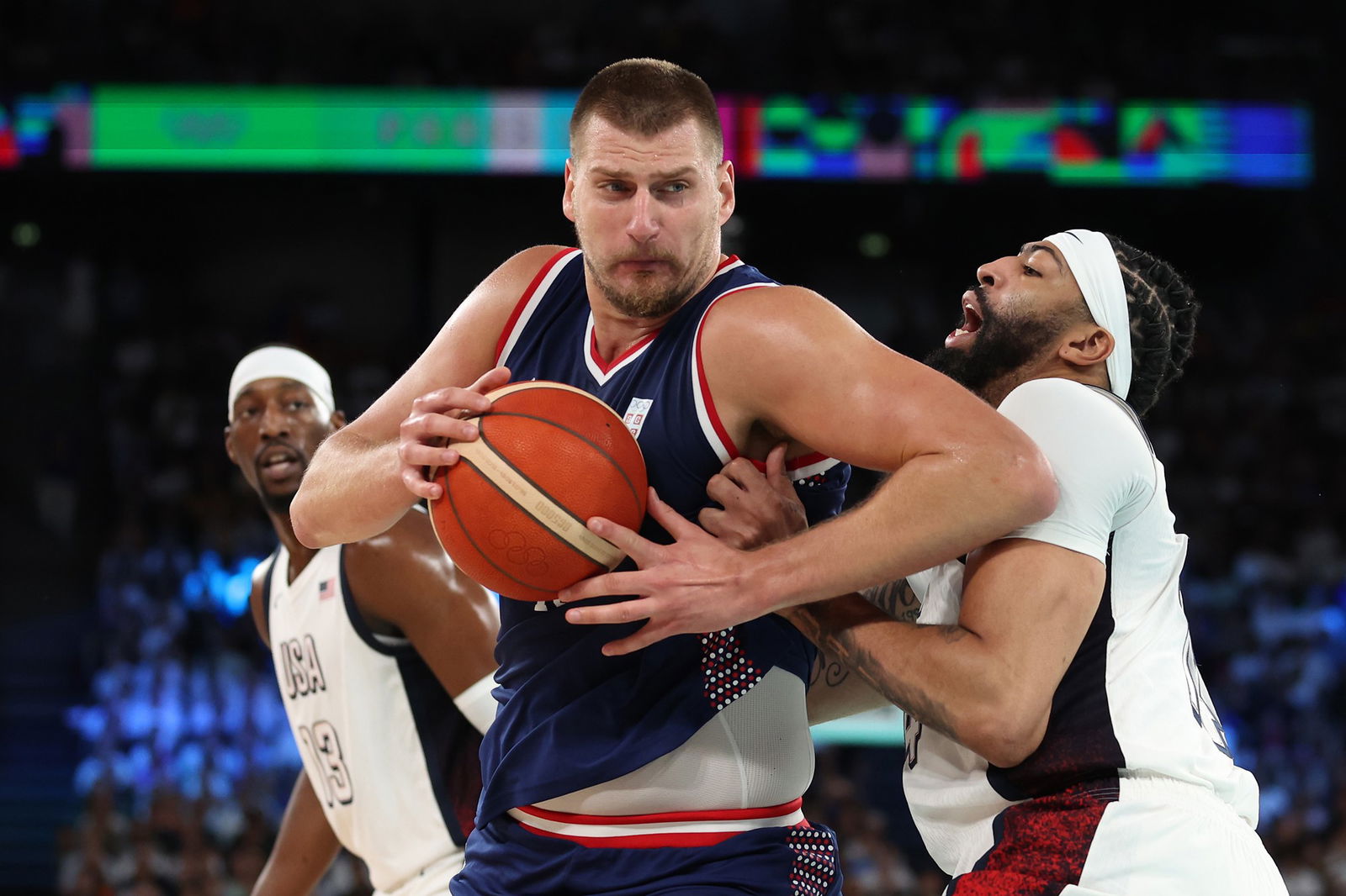 A basketballer in blue holds the ball in a tussle with an opponent in white.