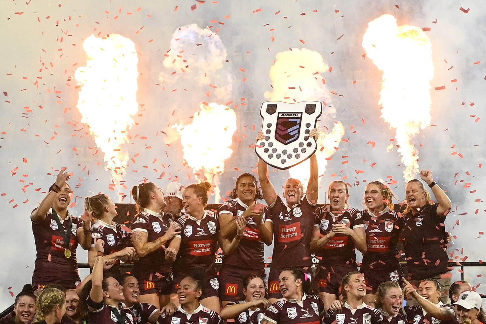 Queensland Maroons lift the Women's State of Origin shield as pyrotechnics go off.