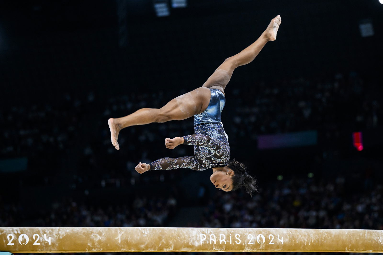 Simone Biles upside down with her legs split as she competes on the balance beam.