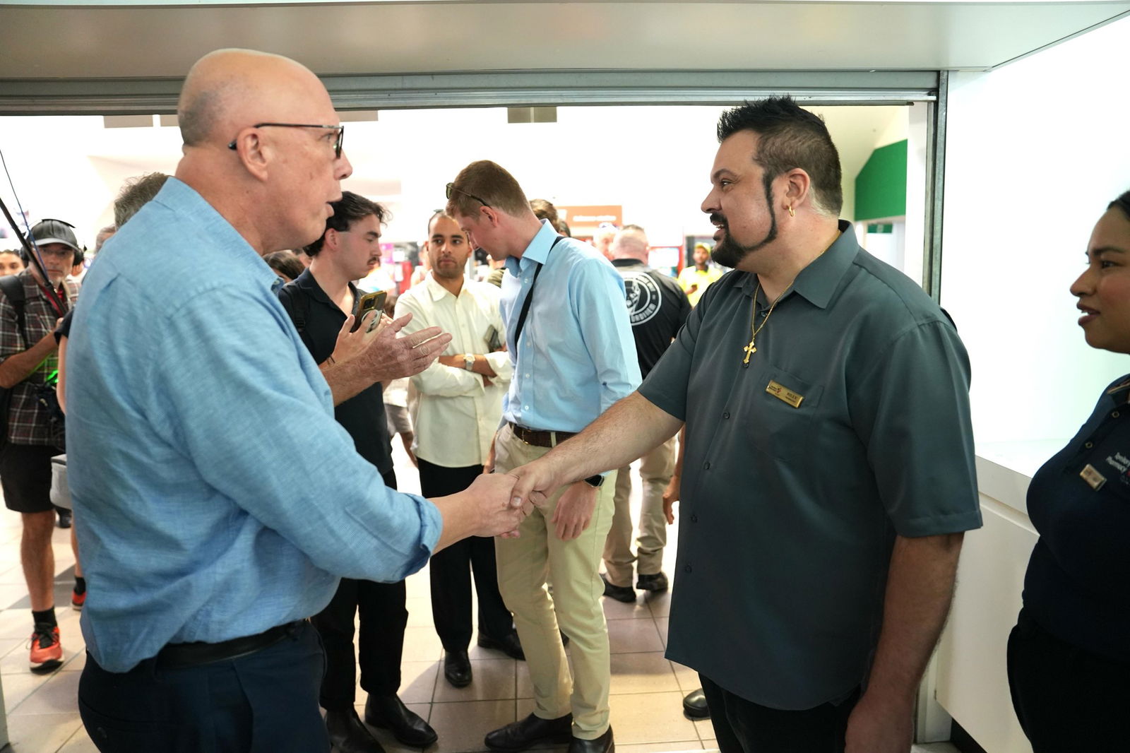 Peter Dutton shakes hands with a middle-aged man in a grey polo shirt.