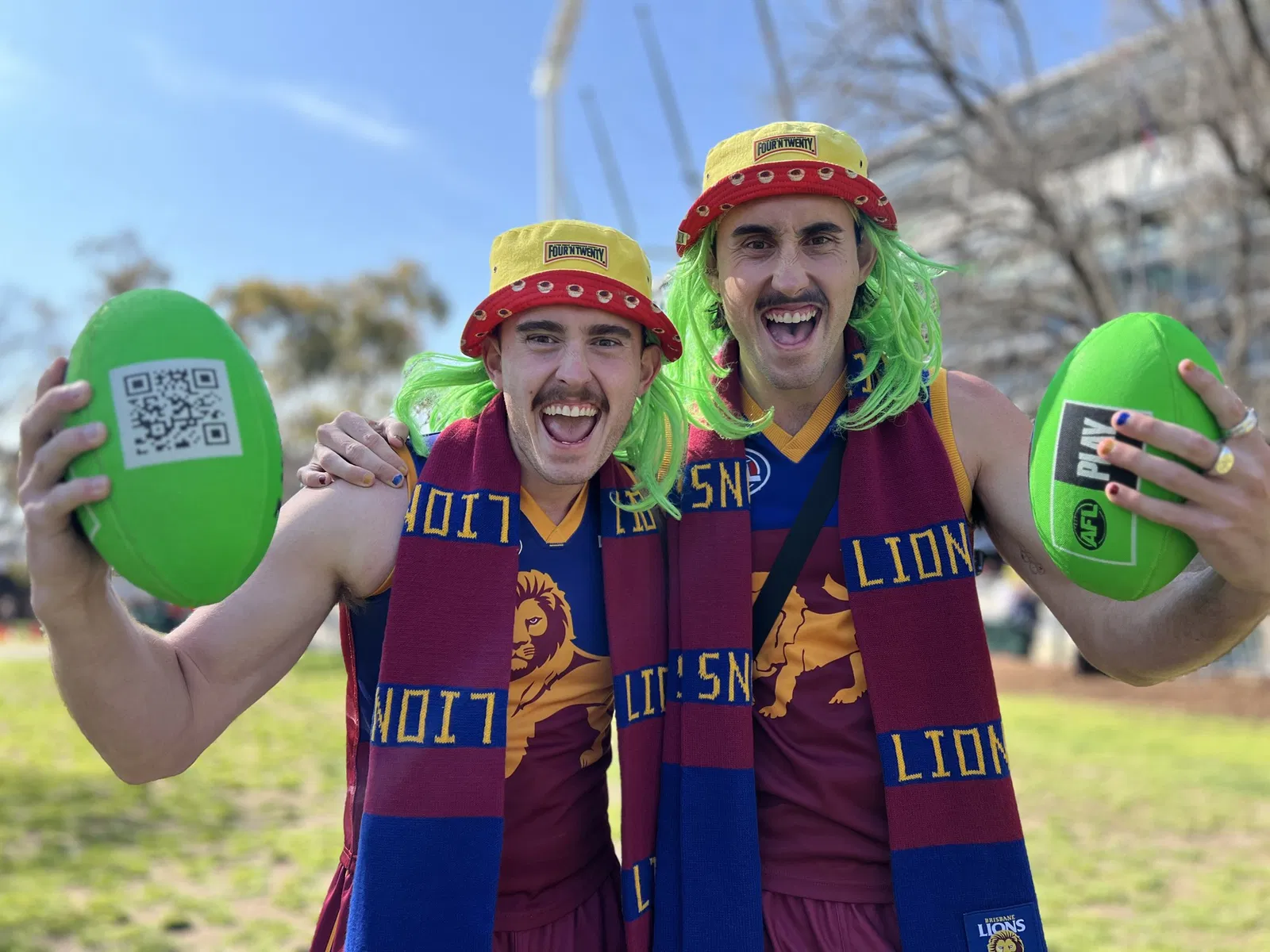 Bailey and Lachlan, dressed from head to toe in Brisbane Lions gear, smile and hold footballs.