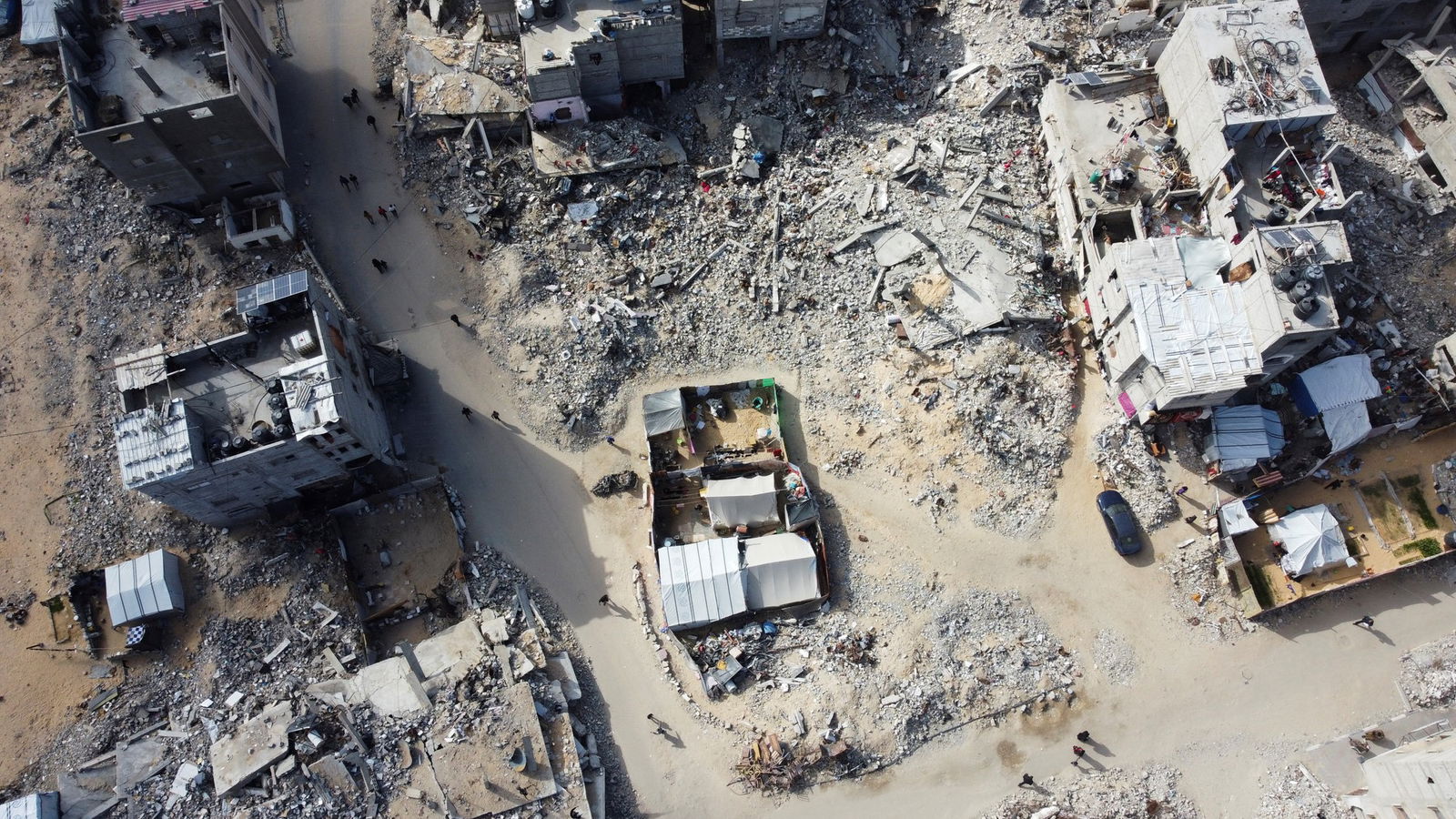 A drone view shows Palestinians walking past the rubble of houses and buildings destroyed in Israeli strikes