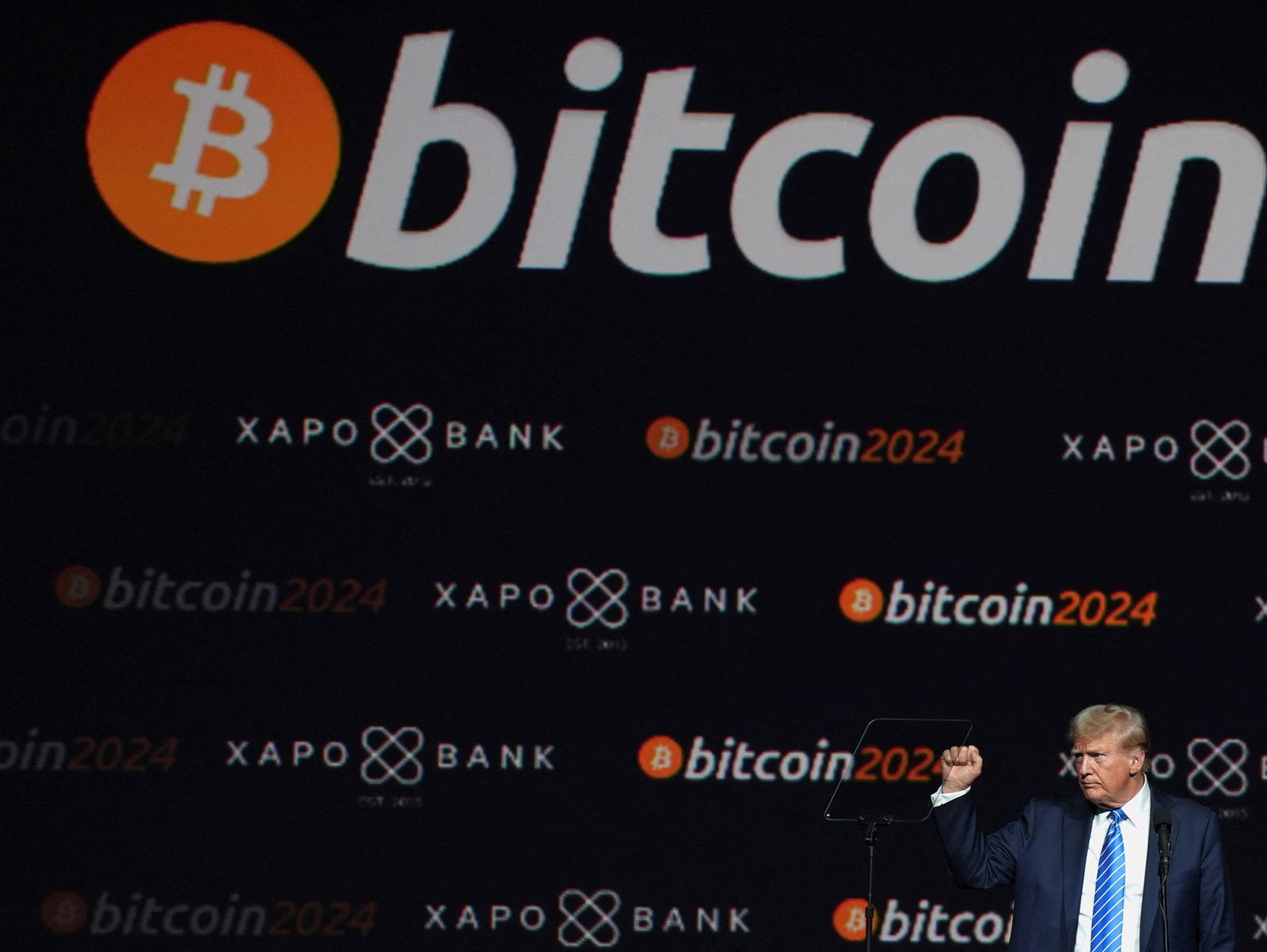 Donald Trump makes a fist in front of a bitcoin backdrop.