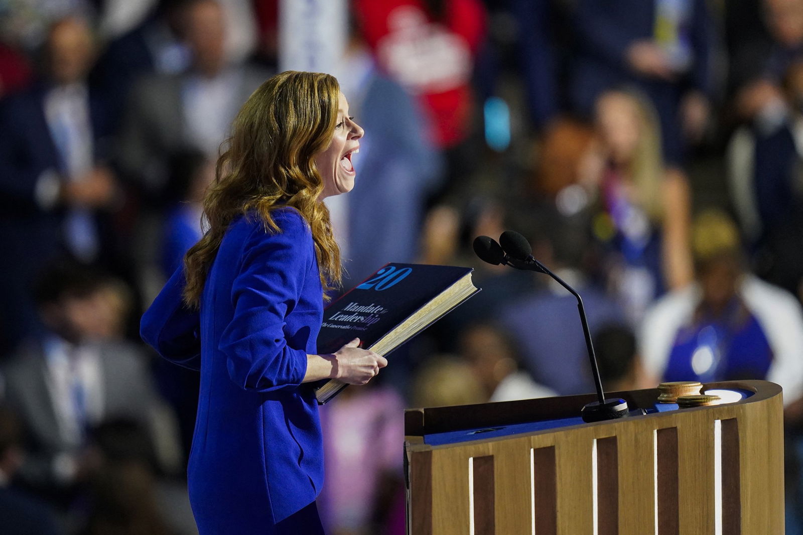 Mallory McMorrow holds a large book against her waist as she speaks at a podium